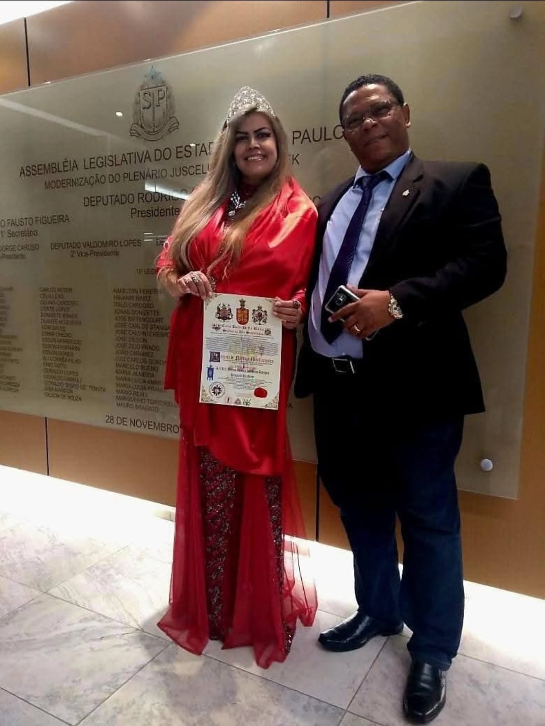 Carlos Alberto Garcia ao lado de uma mulher de vermelho, com o diploma da Casa Della Rosa.