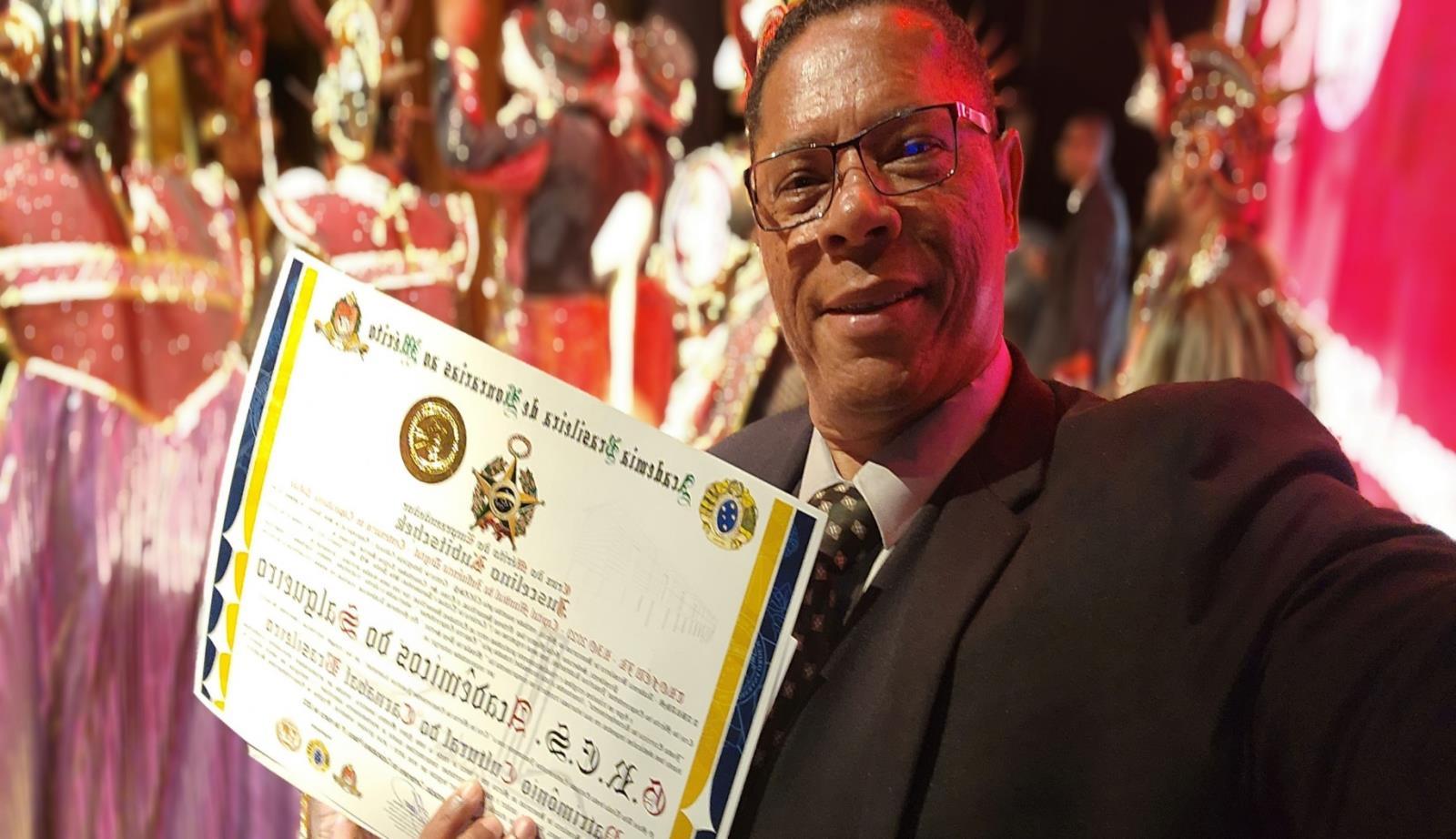 Carlos Alberto Garcia de terno, com um certificado de reconhecimento.